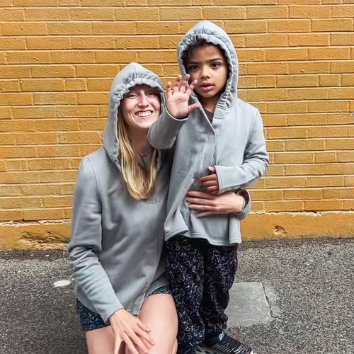 Two people wearing matching Person wearing a Sense-ational You QuietSense Sound Reducing Sensory Grey Hoodies in front of a yellow brick wall