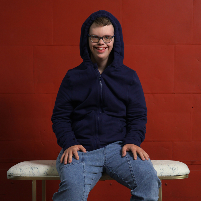 Person wearing a Sense-ational You QuietSense Sound Reducing Sensory Zippered Hoodie on a white bench against a red wall