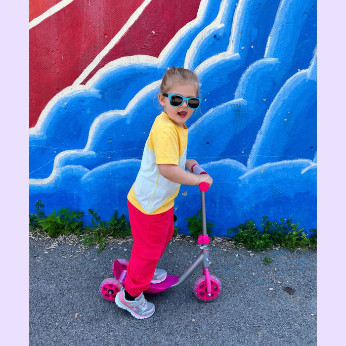 Child on a scooter in front of a colorful wall with blue and red design while wearing a Sense-ational You Sensory Friendly Fidget Youth Coral Joggers