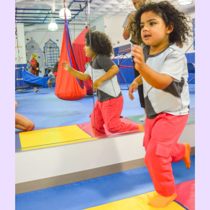 Children playing in a colorful indoor play area while wearing a Sense-ational You Sensory Friendly Fidget Youth Coral Joggers on a white background.