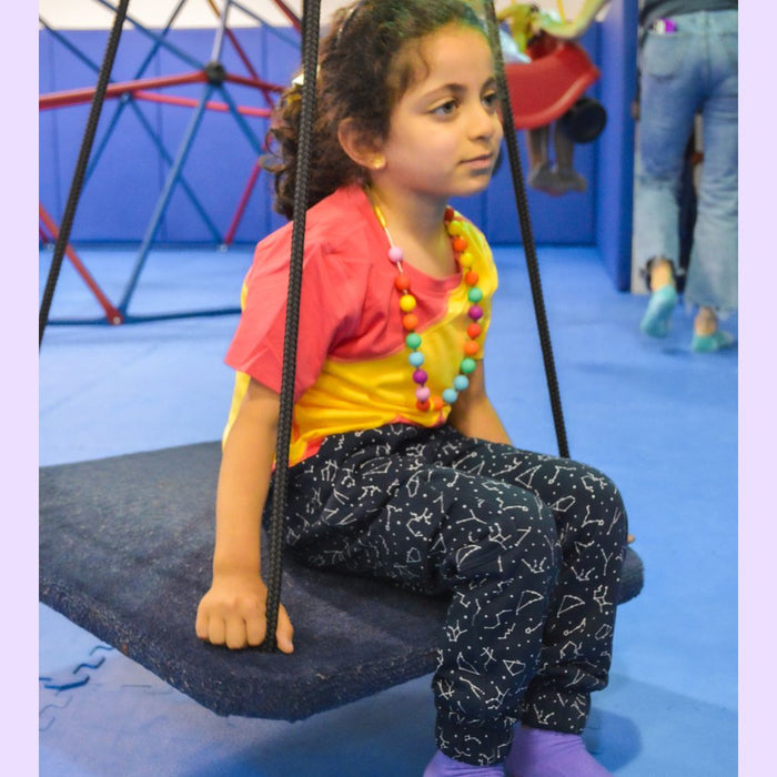 Child wearing a Sense-ational You Sensory Friendly Fidget Youth Constellation Joggers on a swing at an indoor playground