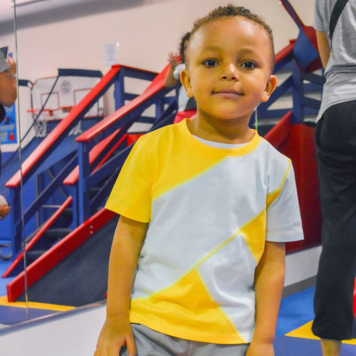 Child wearing a Sense-ational You Sensory Friendly Yellow/Mint Youth T-Shirt in an indoor playground setting