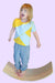 Child standing on a balance board while wearing a Sense-ational You Sensory Friendly Yellow/Mint Youth T-Shirt on a white background