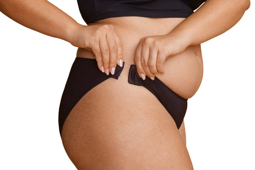 A close-up of a model wearing Slick Chicks Adaptive Bikini Brief Panty in black, pulling the hook & eye side closures closed with both hands, against a plain white background