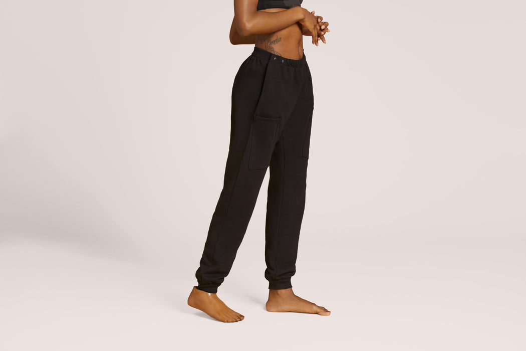 Side angle of a model wearing Slick Chicks Adaptive Fitted Lounge Joggers in black against a beige background