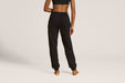 Back angle of a model wearing Slick Chicks Adaptive Fitted Lounge Joggers in black against a beige background