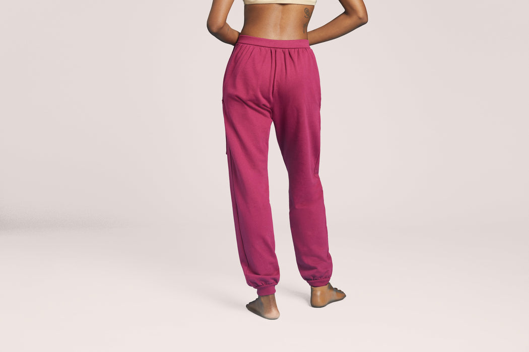 Back angle of a model wearing Slick Chicks Adaptive Fitted Lounge Joggers in plum against a beige background