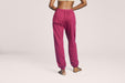 Back angle of a model wearing Slick Chicks Adaptive Fitted Lounge Joggers in plum against a beige background