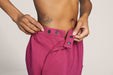 Close up of a model wearing Slick Chicks Adaptive Fitted Lounge Joggers in plum, demonstrating the clasp button openings by pulling the waist band off of the clasp buttons, against a beige background