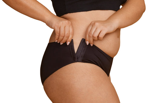 Close-up of a model wearing Slick Chicks Adaptive Hipster Panty in black, pulling the hook & eye side closures with both hands against a plain white background