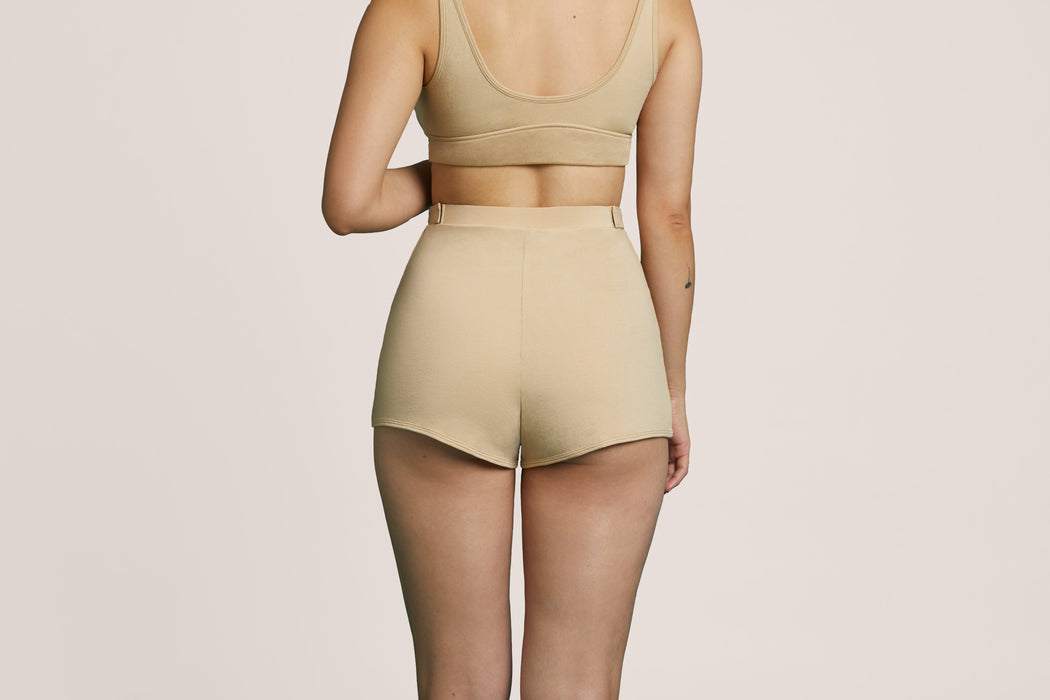 Back angle of a model wearing Slick Chicks Adaptive Lounge Short in beige against a beige background