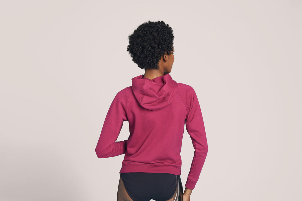 Back angle of a model wearing the Slick Chicks Adaptive Magnetic Zip-Up Hoodie in plum against a beige background