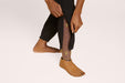 Close up of a model wearing Slick Chicks Adaptive Side Zip Joggers in black, unzipping the side of the jogger which shows their prosthetic leg, against a plain beige background