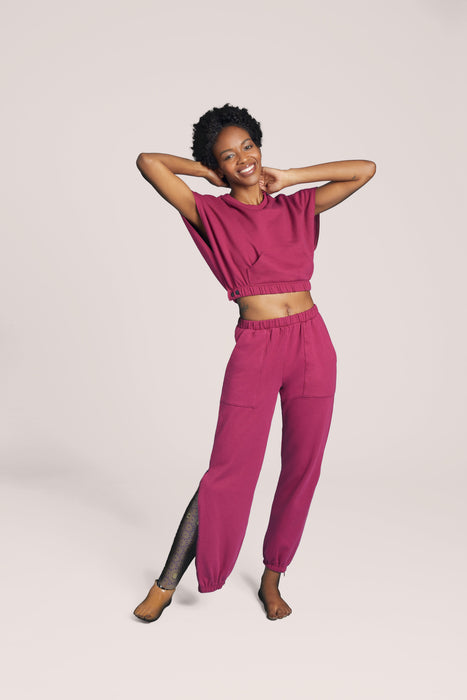 A model posing in matching Slick Chicks Adaptive V-Neck Crop Top and Adaptive Side Zip Joggers in plum against a plain beige background