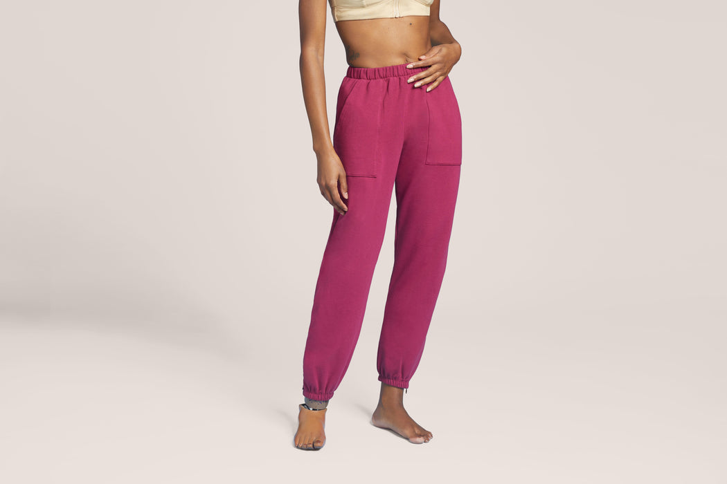 Front angle of a model wearing Slick Chicks Adaptive Side Zip Joggers in plum against a plain beige background