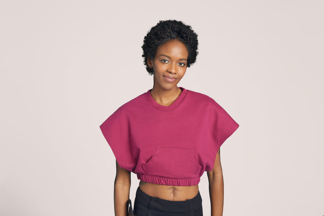 Front angle of a woman with short curly black hair wearing Slick Chicks Adaptive V-Neck Crop Top in plum, against a solid beige background