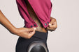 Close-up of a Side angle of a model wearing Slick Chicks Adaptive V-Neck Crop Top in plum, demonstrating the clasp button openings against a solid beige background