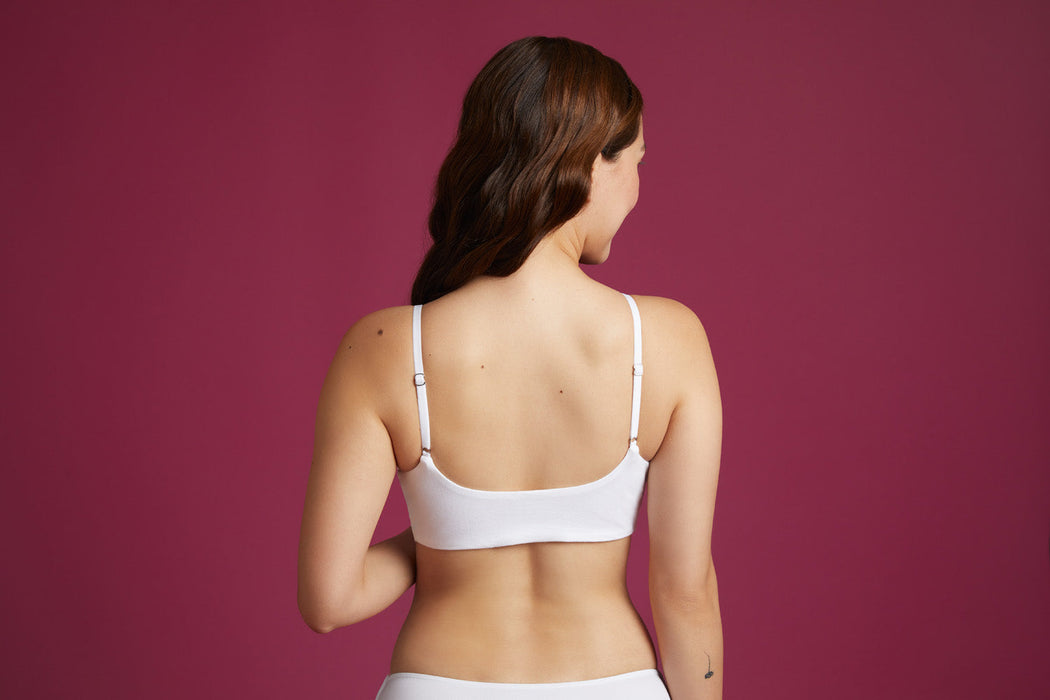 Back angle of a model wearing Slick Chicks Adaptive Wireless Front Fastening Bra in white against a plum background