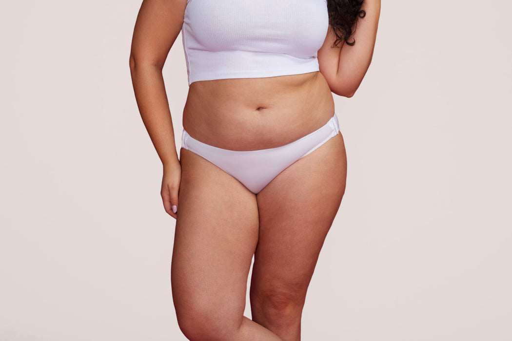 Front angle of a model wearing Slick Chicks Adaptive Bikini Brief Panty in white against a plain light beige studio background