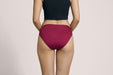 Back angle of a model wearing Slick Chicks Adaptive Bikini Brief Panty in plum against a plain light beige studio background