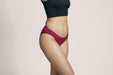 Side angle of a model wearing Slick Chicks Adaptive Bikini Brief Panty in plum against a plain light beige studio background