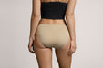 Back angle of a model wearing Slick Chicks Adaptive Bikini Brief Panty in beige against a plain light beige studio background