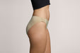 Side angle of a model wearing Slick Chicks Adaptive Bikini Brief Panty in beige against a plain light beige studio background