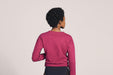 Back angle of a woman with short black curly hair wearing Slick Chicks Adaptive Crewneck Sweatshirt in plum, against a solid beige background