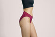 Side angle of a model wearing Slick Chicks Adaptive High Waist Brief in plum against a plain light beige studio background