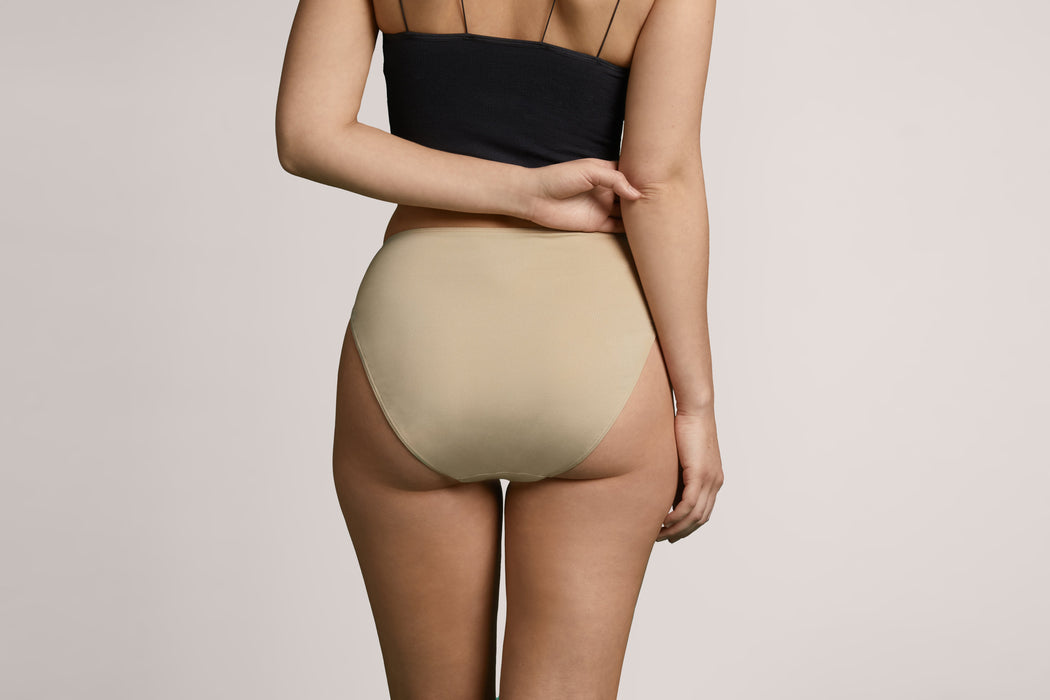 Rear angle of a model wearing Slick Chicks Adaptive High Waist Brief in beige against a plain light beige studio background