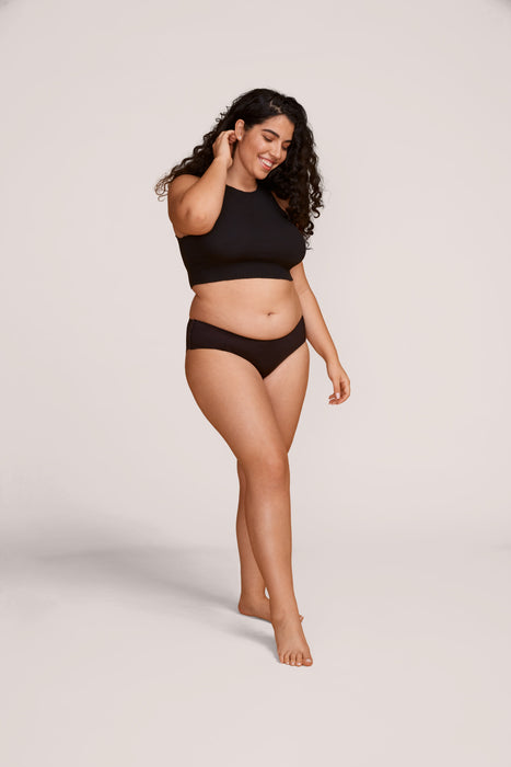 A woman modeling Slick Chicks Adaptive Hipster Panty in black against a plain light beige studio background