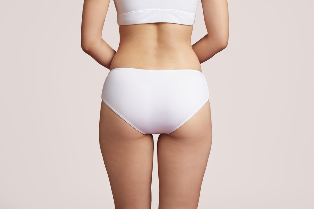 Back angle of a model wearing Slick Chicks Adaptive Hipster Panty in white against a plain light beige studio background