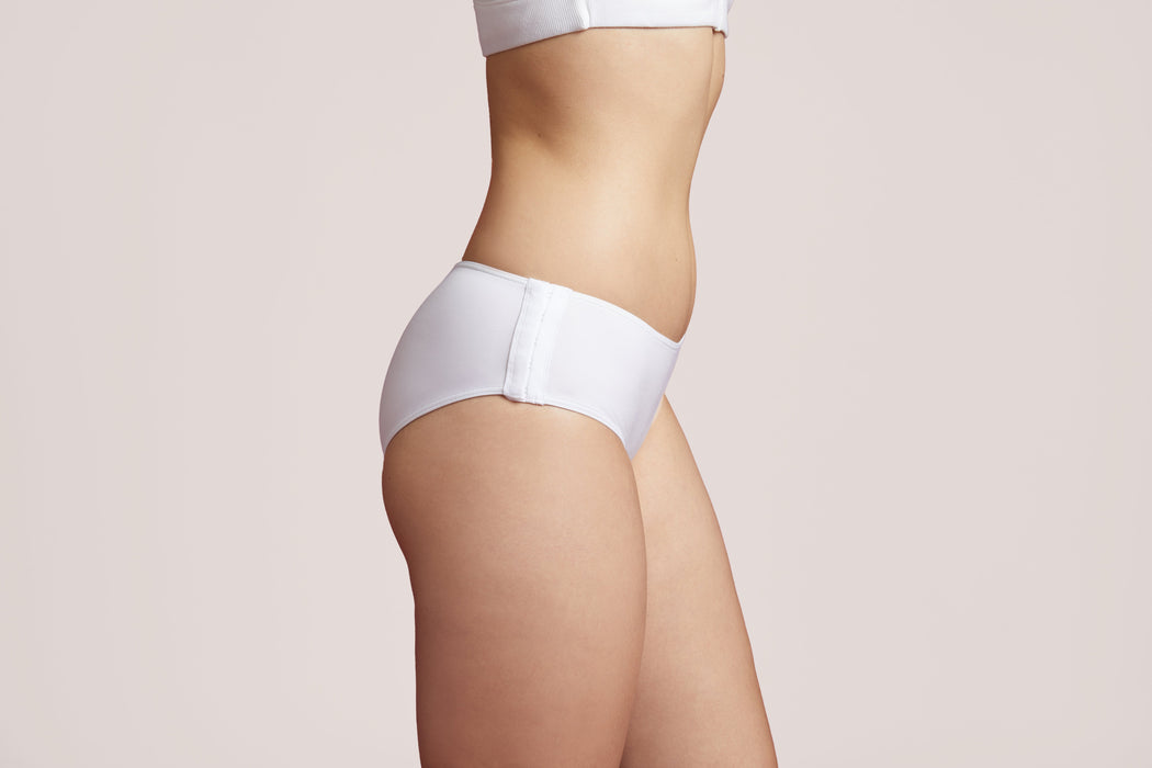 Side angle of a model wearing Slick Chicks Adaptive Hipster Panty in white against a plain light beige studio background