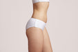 Side angle of a model wearing Slick Chicks Adaptive Hipster Panty in white against a plain light beige studio background