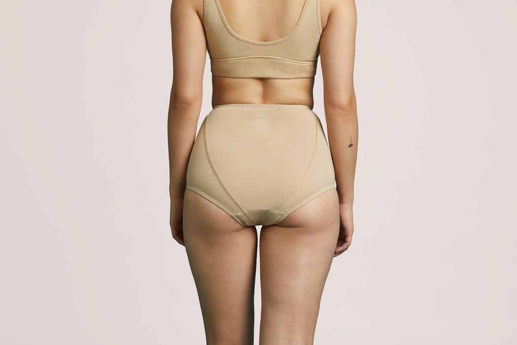 Back angle of a model wearing Slick Chicks Adaptive Leakproof Underwear in beige against a plain light beige studio background