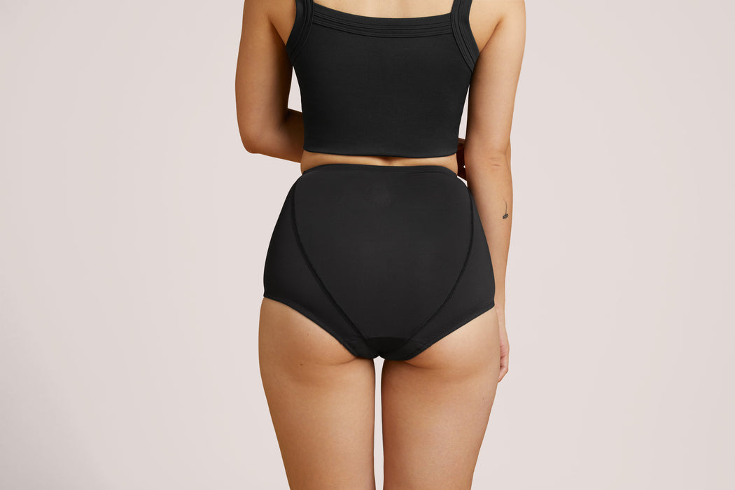 Back angle of a model wearing Slick Chicks Adaptive Leakproof Underwear in black against a plain light beige studio background