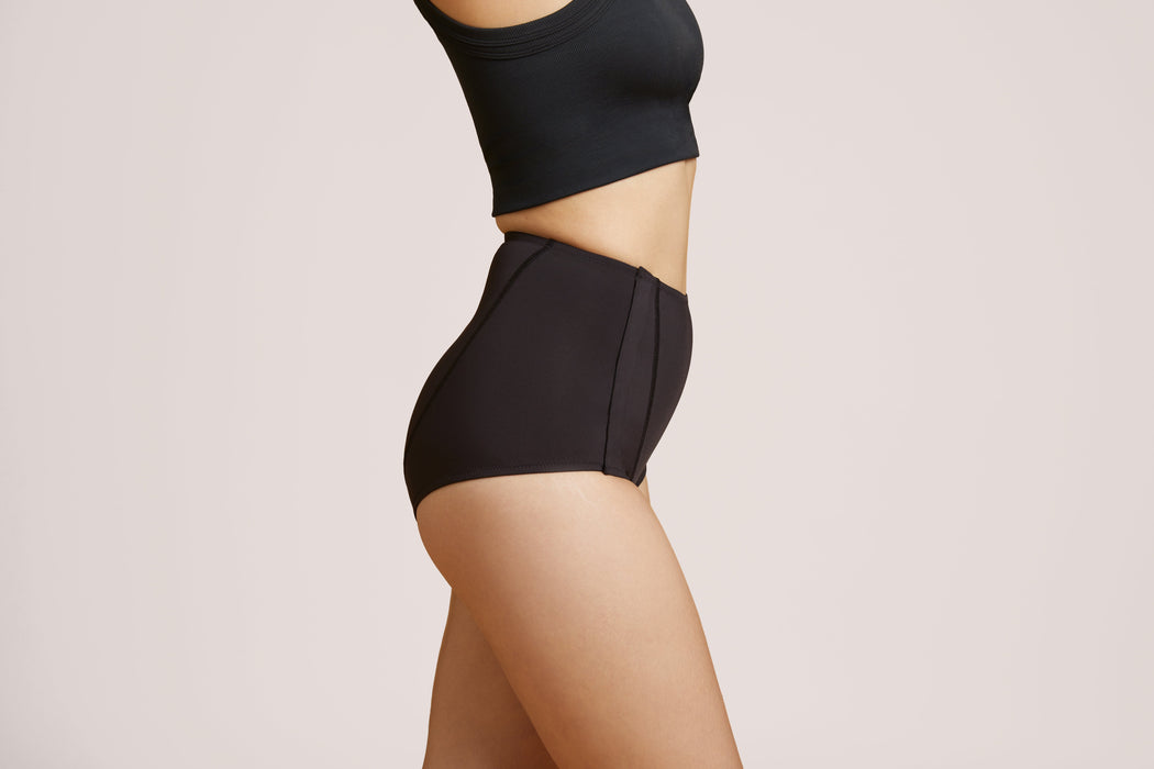 Side angle of a model wearing Slick Chicks Adaptive Leakproof Underwear in black against a plain light beige studio background