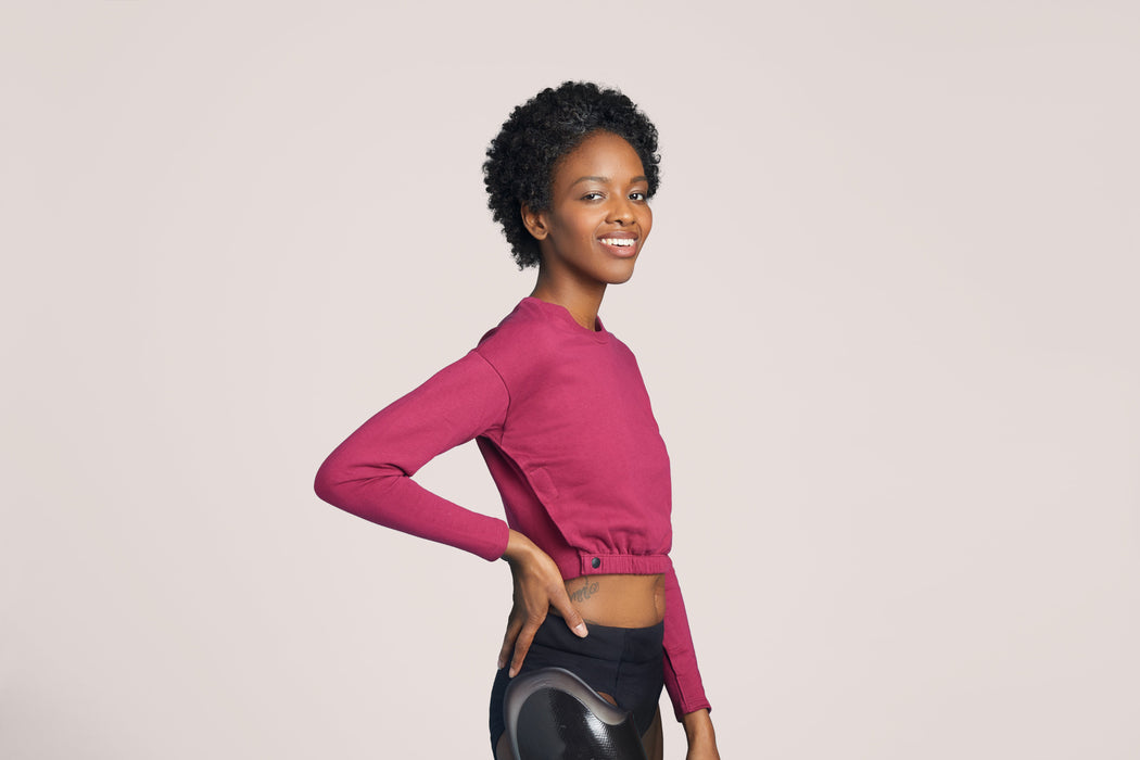 Side angle of a smiling woman with short curly black hair wearing Slick Chicks Adaptive Long Sleeve Lounge Shirt in plum, against a solid beige background