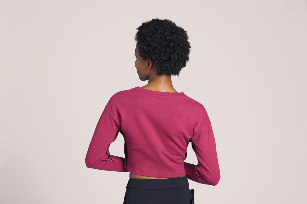 Back angle of a smiling woman with short curly black hair looking to the side wearing Slick Chicks Adaptive Long Sleeve Lounge Shirt in plum, against a solid beige background