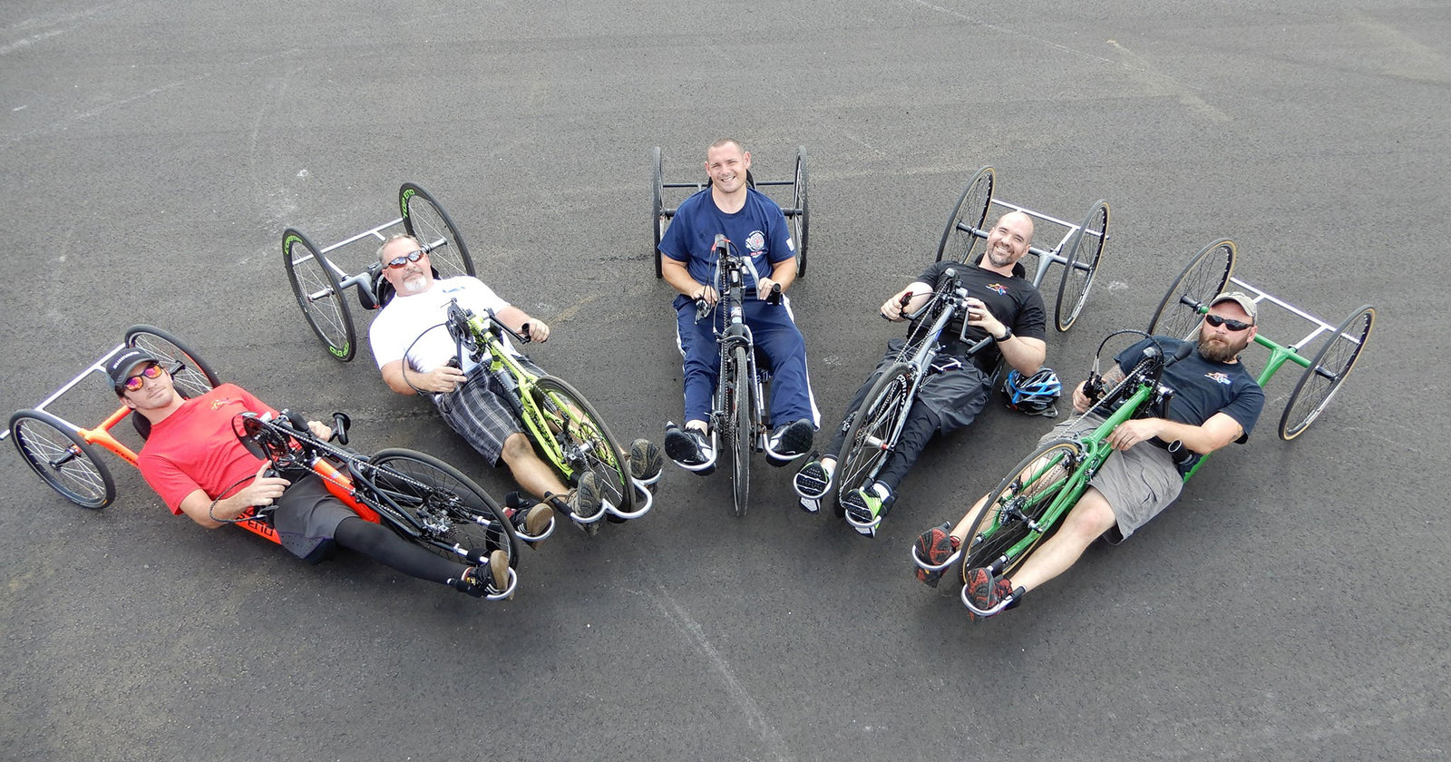 Five people sitting on Top End Handcyclesin a circle on a paved surface.