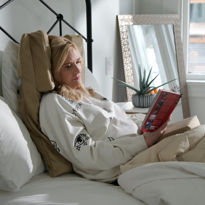 Woman reading a book in bed with a cozy atmosphere being supported by the Tausi Pillow System