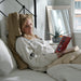 Woman reading a book in bed with a cozy atmosphere being supported by the Tausi Pillow System