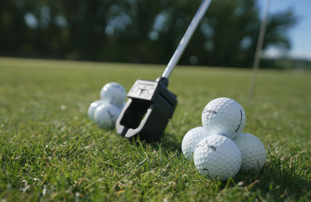 Detail of Tee Tender Adaptive Golf Ball Teeing Device tip next to golf balls on a golf course
