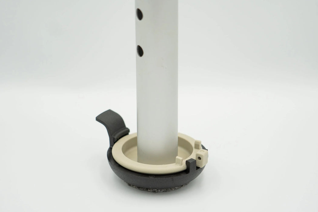 Versa Coast walker footing installed on a silver walker leg, with the tan base puck seated in the black coaster and its quick release tab, on a white background