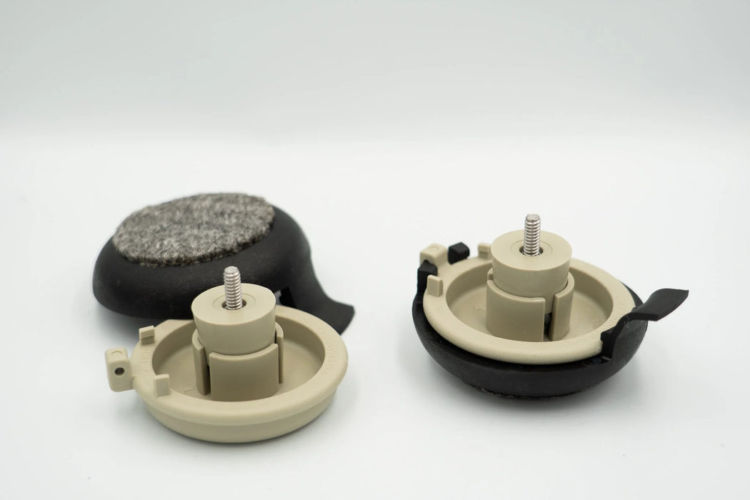 Two Versa Coast tan base pucks with expansion inserts and screws, one snapped into a black coaster and one beside a black coaster showing its gray carpeted pad