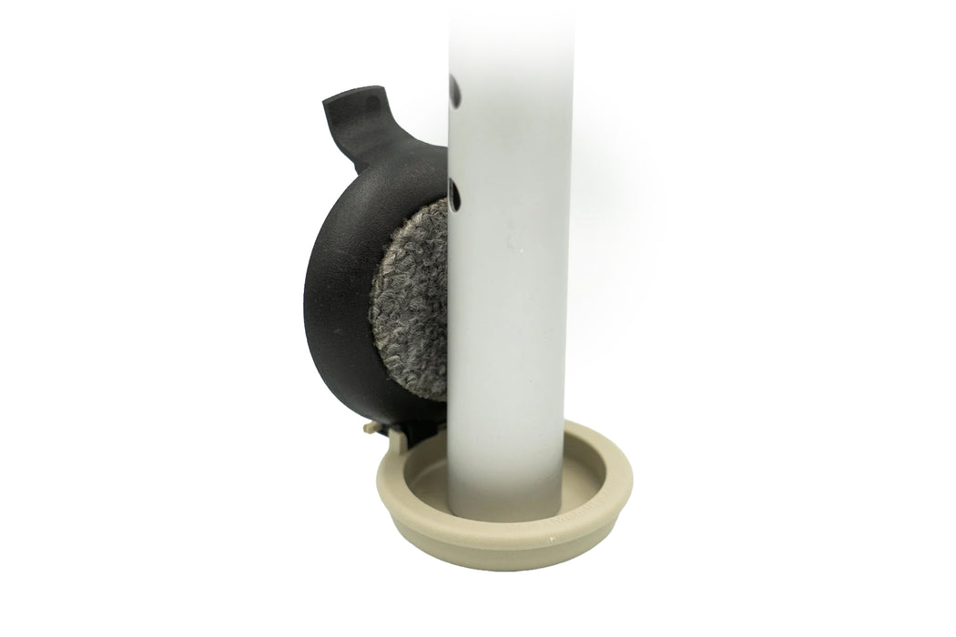 Versa Select black coaster flipped up on its hinge beside a silver walker leg, showing its gray carpeted pad above the tan base puck on a white background