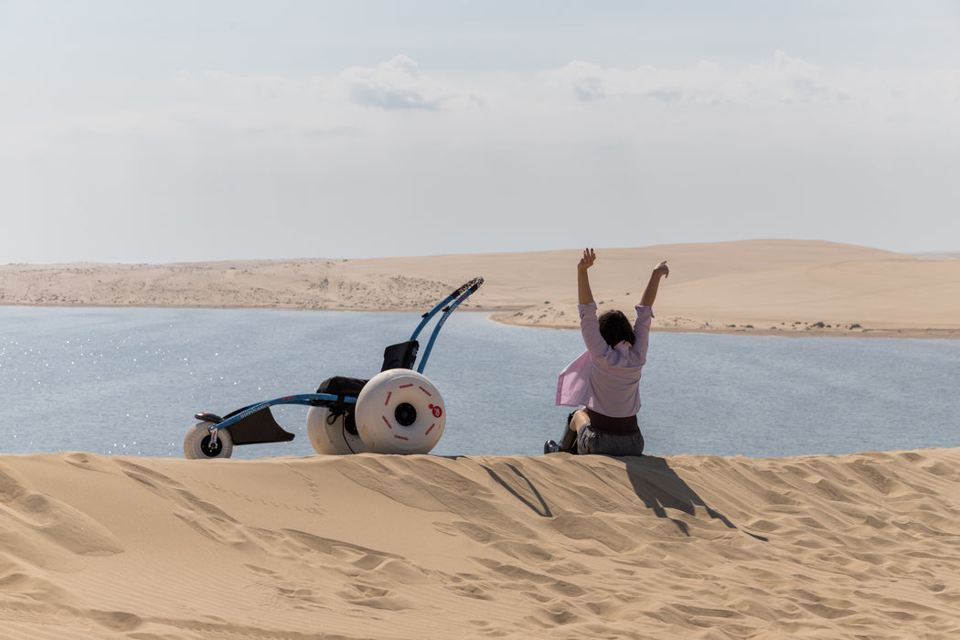 Person with arms raised on a sand dune overlooking a lake.