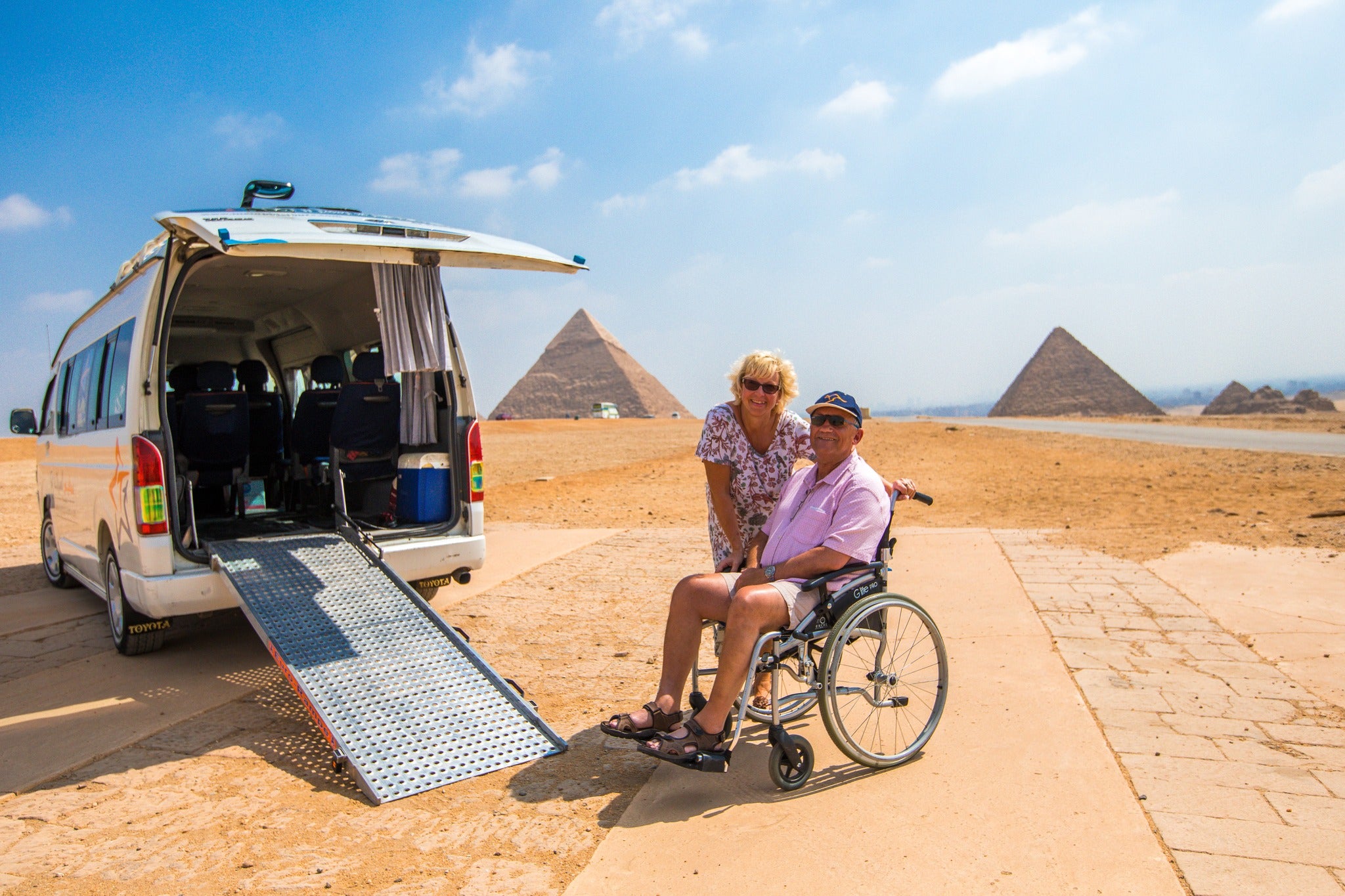 Person using a wheelchair about to enter a van with pyramids in the background