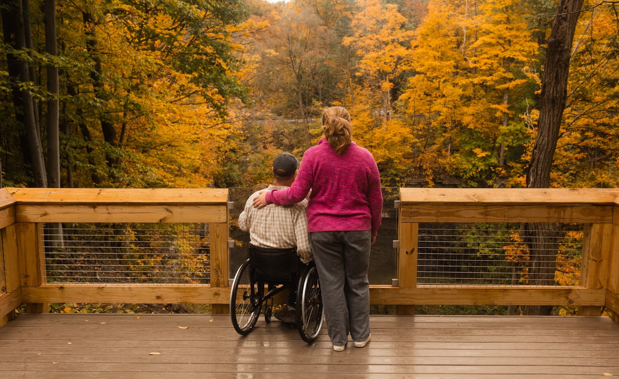 Two people on a wooden deck with a backdrop of autumn trees.