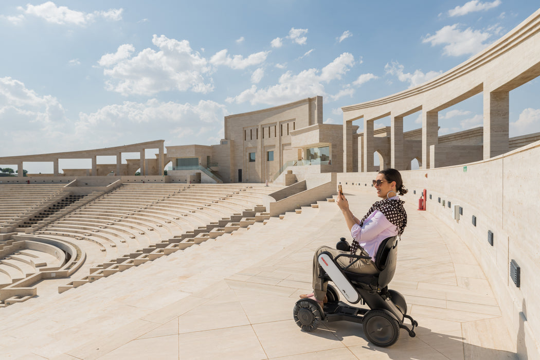 Person using a mobility device in an outdoor setting with architectural background.